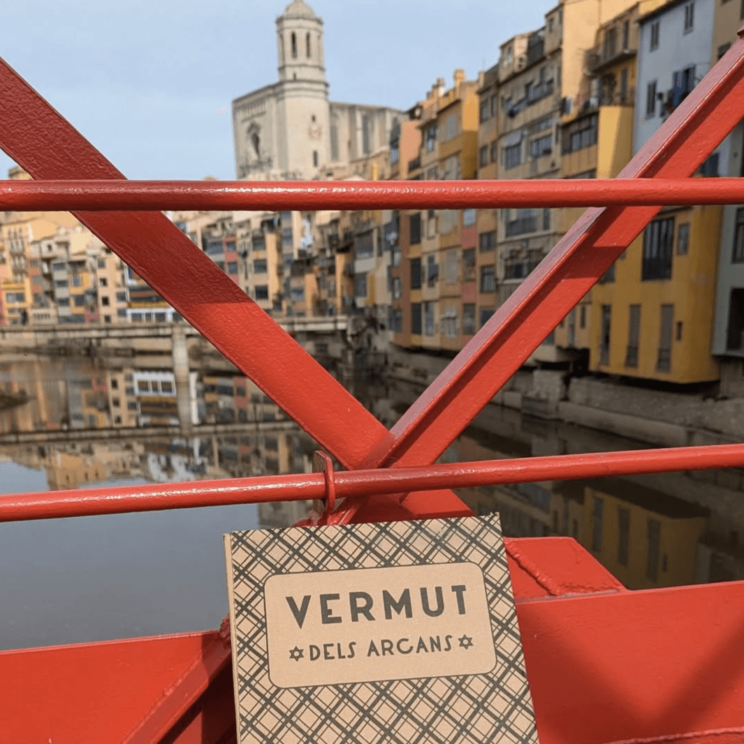 Etiqueta Vermut dels Arcans penjada a la barana vermella del pont de Girona